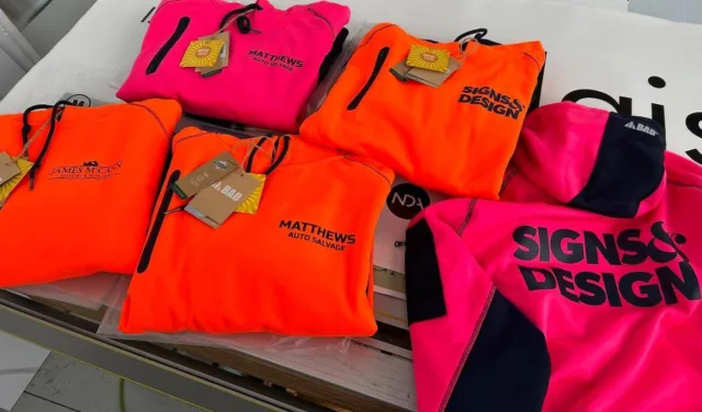 Fluorescent orange and pink hoodies with embroidered company logos and Signs & Design branding