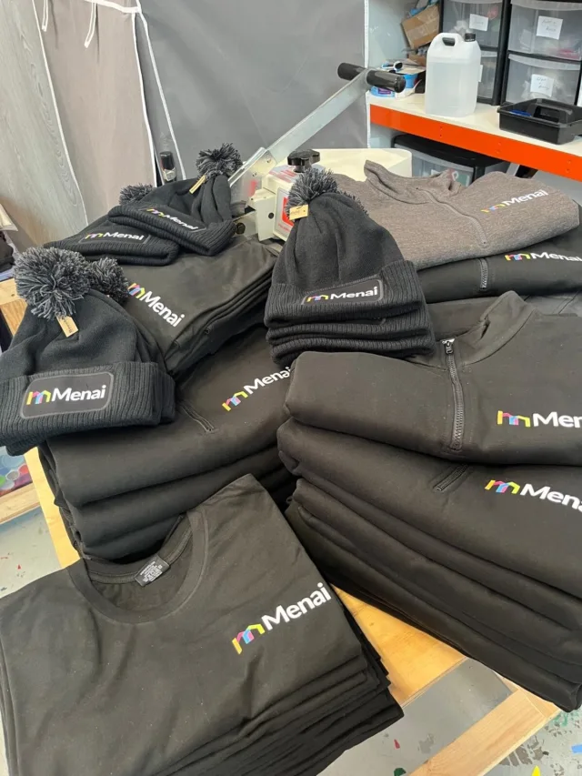 Branded workwear including embroidered hats, sweatshirts, and T-shirts with Menai logo